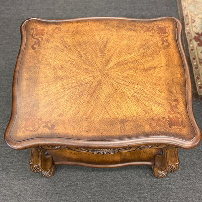 A traditional carved wood end table featuring ornate acanthus leaf aprons, cabriole legs, a sunburst wood veneer top, and a bottom display shelf in good condition.