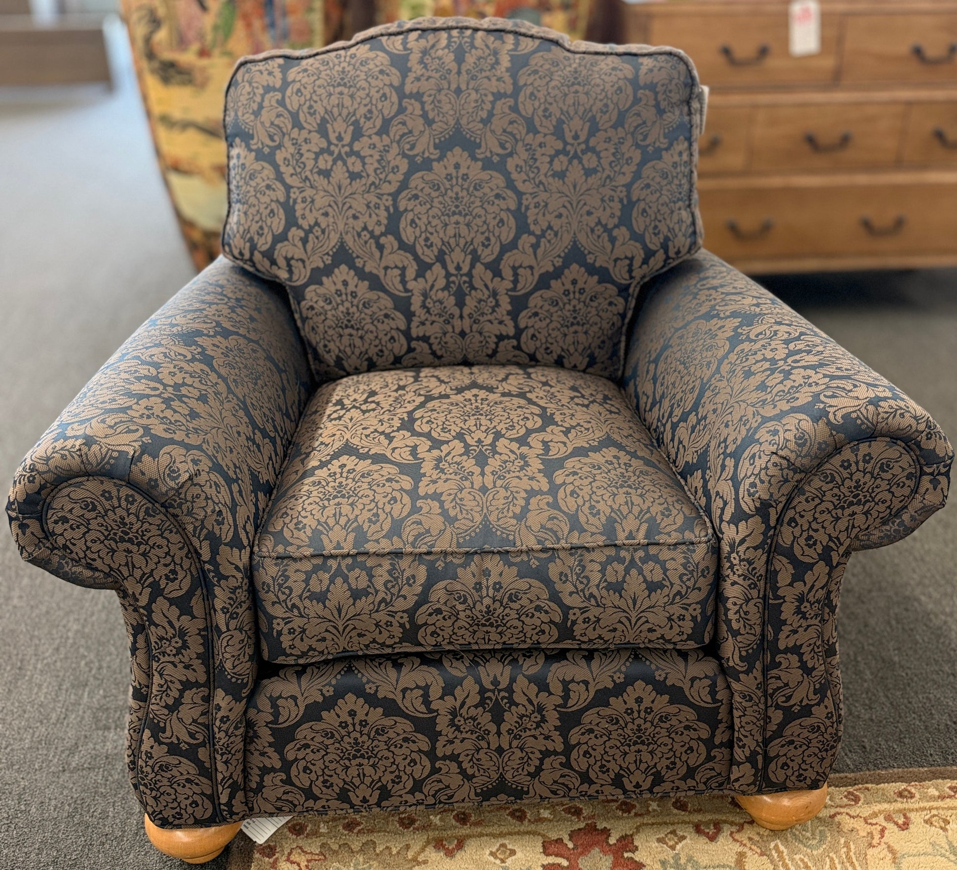 traditional plush armchair featuring rolled arms and upholstered in a dark blue and brown damask pattern on a wooden frame.