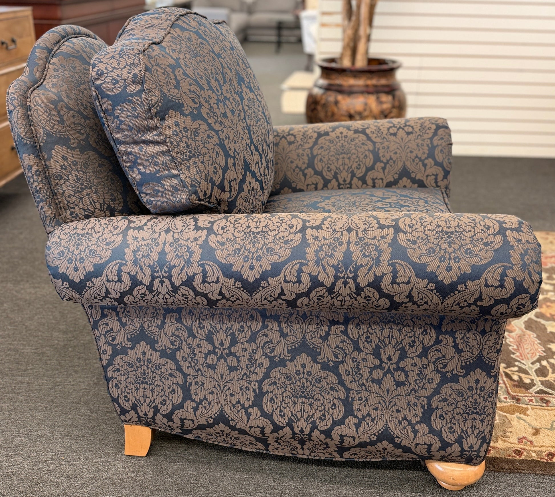 A traditional plush armchair featuring rolled arms and upholstered in a dark blue and brown damask pattern on a wooden frame.