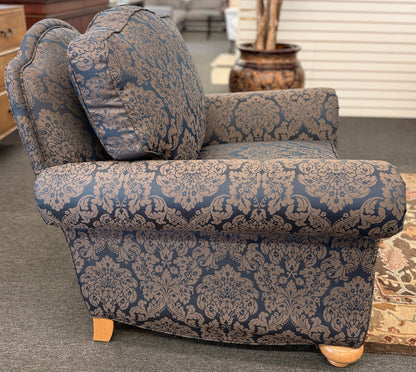 A traditional plush armchair featuring rolled arms and upholstered in a dark blue and brown damask pattern on a wooden frame.