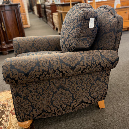 A traditional plush armchair featuring rolled arms and upholstered in a dark blue and brown damask pattern on a wooden frame.