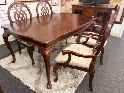 A traditional dark wood dining set including a rectangular table and four chairs with ornate backrests and light upholstered seats in excellent condition.