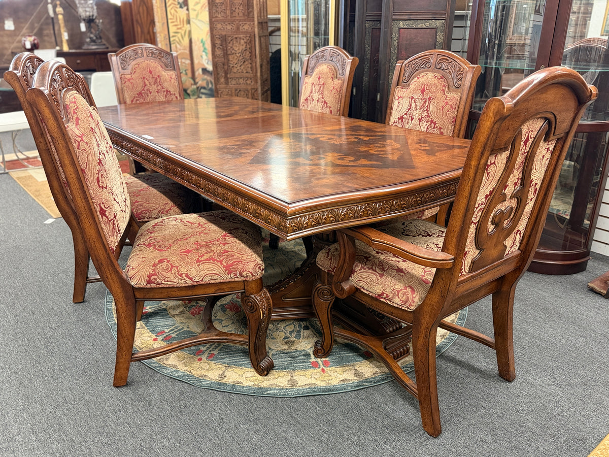 An ornate traditional dark wood dining table with wood-inlay details surrounded by six matching high-back chairs upholstered in red and gold damask fabric in excellent condition.