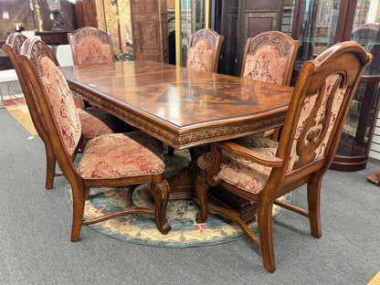 An ornate traditional dark wood dining table with wood-inlay details surrounded by six matching high-back chairs upholstered in red and gold damask fabric in excellent condition.