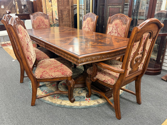 An ornate traditional dark wood dining table with wood-inlay details surrounded by six matching high-back chairs upholstered in red and gold damask fabric in excellent condition.