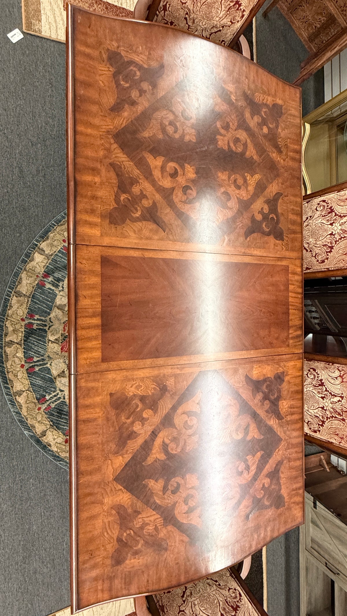 An ornate traditional dark wood dining table with wood-inlay details surrounded by six matching high-back chairs upholstered in red and gold damask fabric in excellent condition.