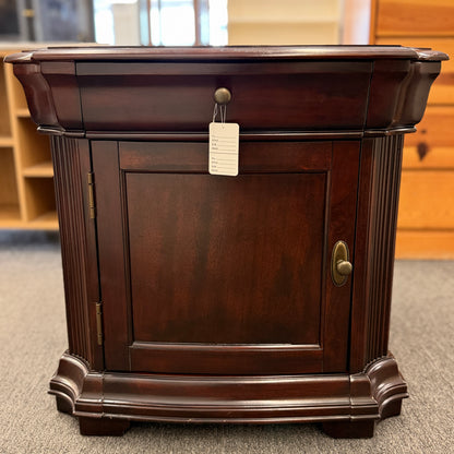 Traditional dark wood nightstand featuring a top drawer, lower cabinet door, fluted corner details, and a classic timeless design.