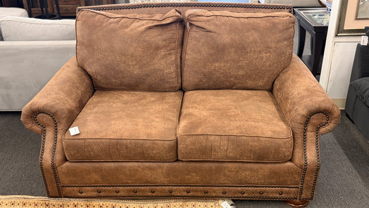 A traditional brown distressed loveseat featuring plush back cushioning, rolled armrests, and deep seating in good condition.