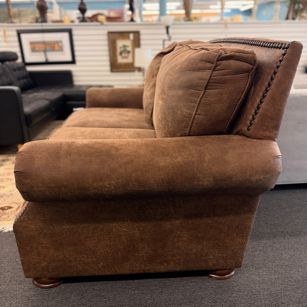 A traditional brown distressed loveseat featuring plush back cushioning, rolled armrests, and deep seating in good condition.