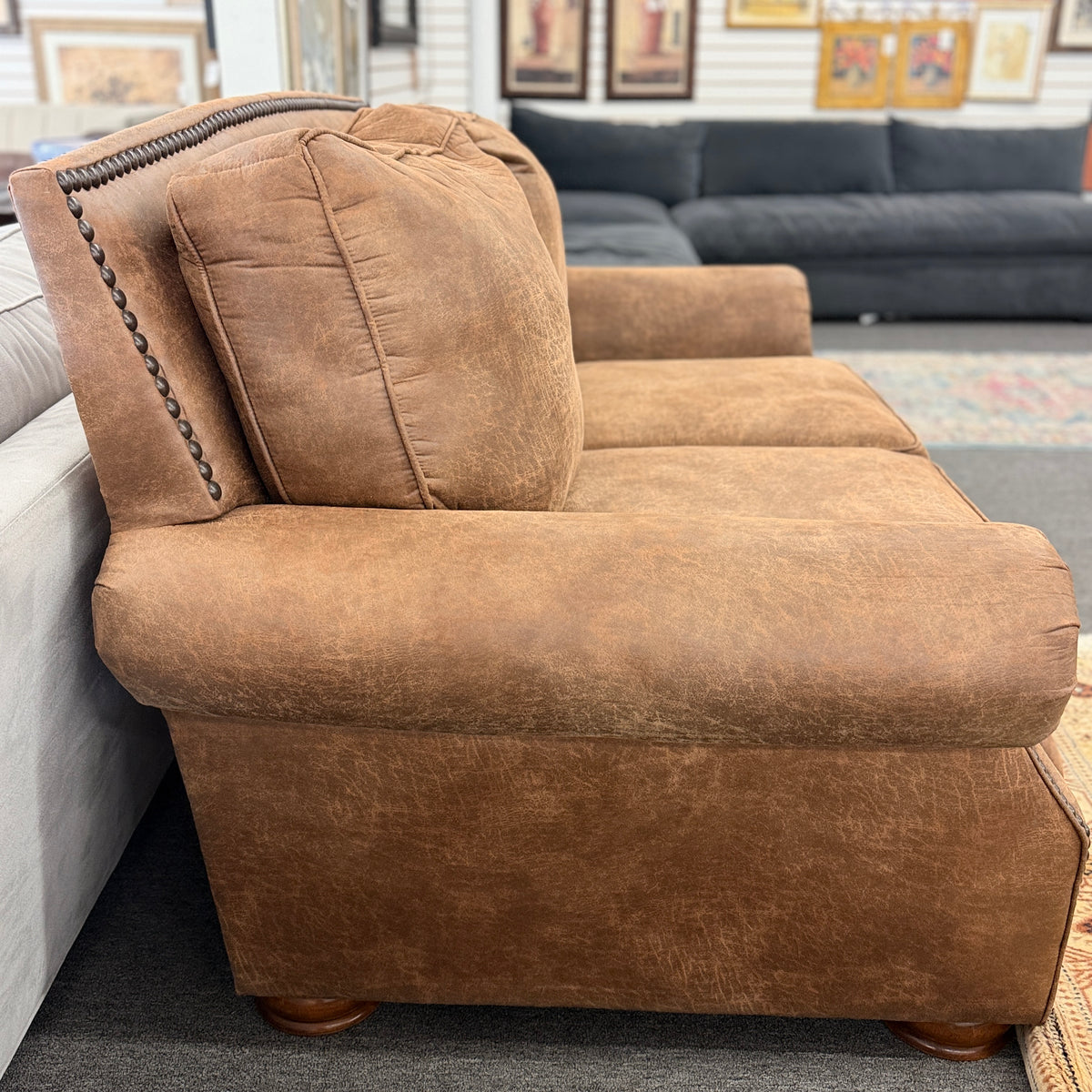 A traditional brown distressed loveseat featuring plush back cushioning, rolled armrests, and deep seating in good condition.