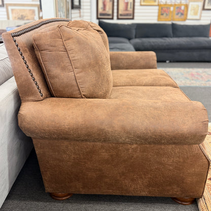 A traditional brown distressed loveseat featuring plush back cushioning, rolled armrests, and deep seating in good condition.