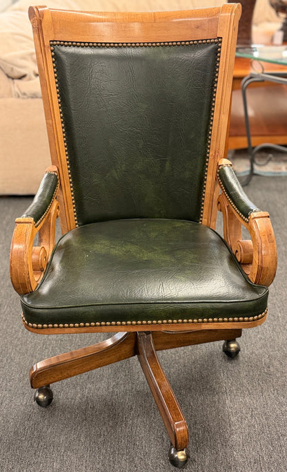 A traditional executive-style office desk chair with polished wood frame, deep forest green faux leather upholstery, brass nailhead trim, and a wheeled swivel base.