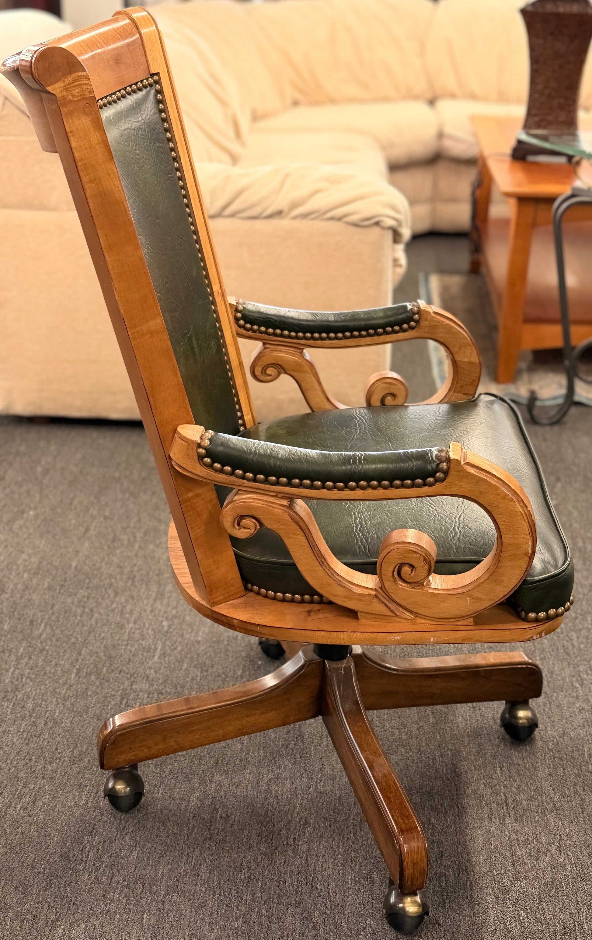 A traditional executive-style office desk chair with polished wood frame, deep forest green faux leather upholstery, brass nailhead trim, and a wheeled swivel base.