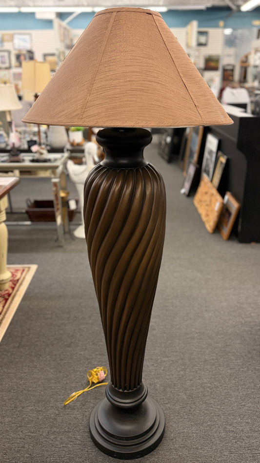 A tall floor lamp featuring a dark twisted pedestal base and a wide tan-colored fabric shade in excellent condition.