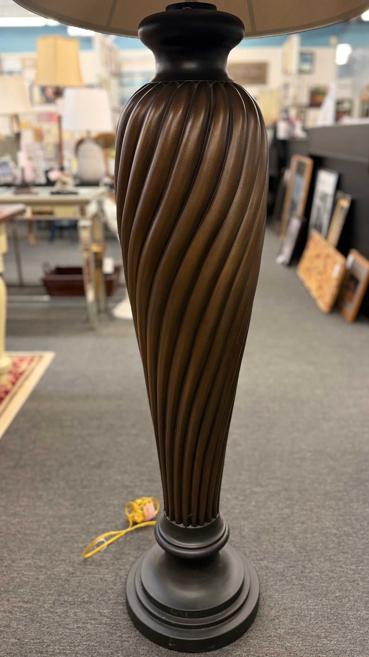 A tall floor lamp featuring a dark twisted pedestal base and a wide tan-colored fabric shade in excellent condition.