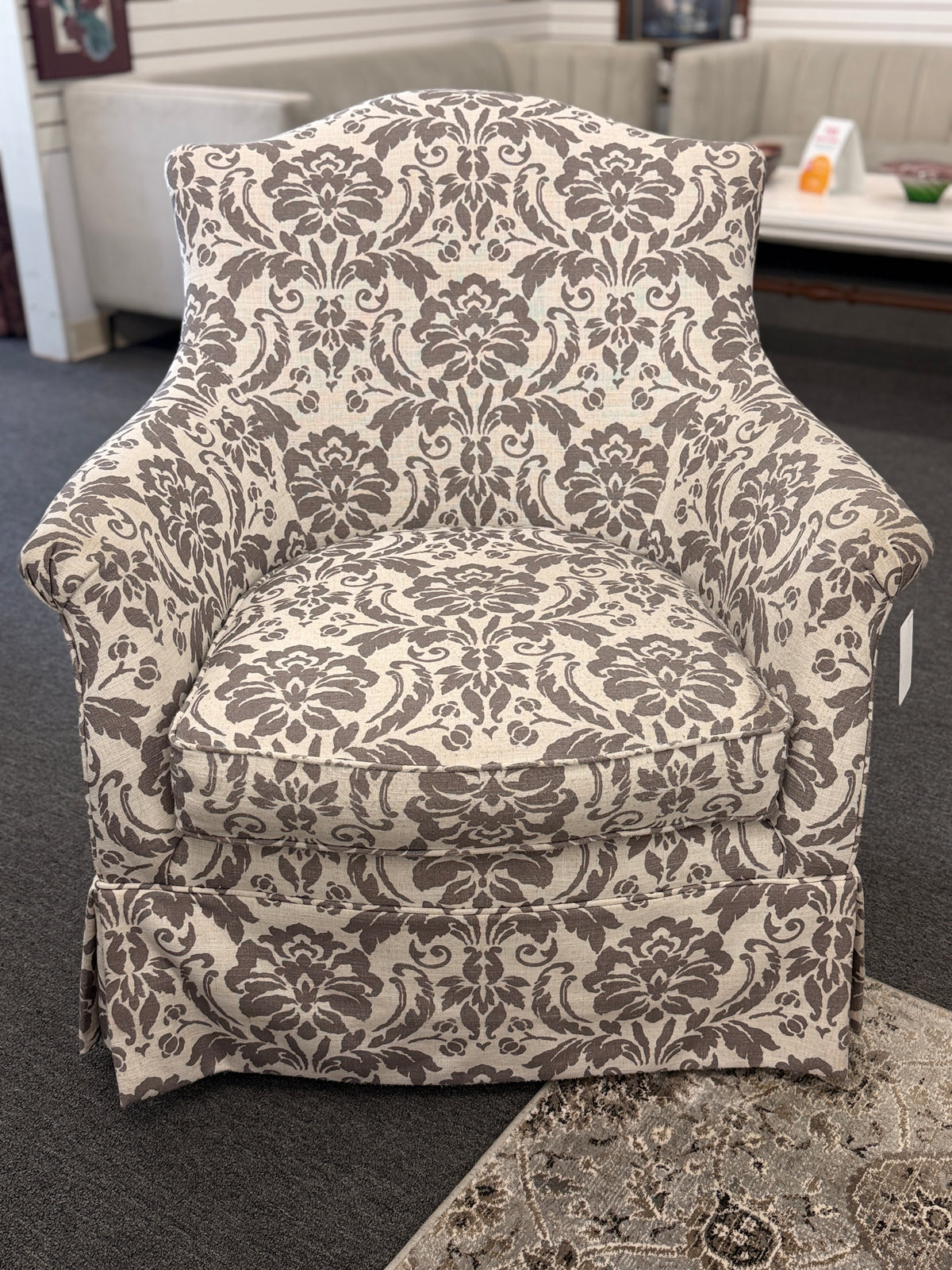 A traditional swivel armchair upholstered in a bold gray-and-cream floral damask pattern featuring a tailored base skirt in good condition.