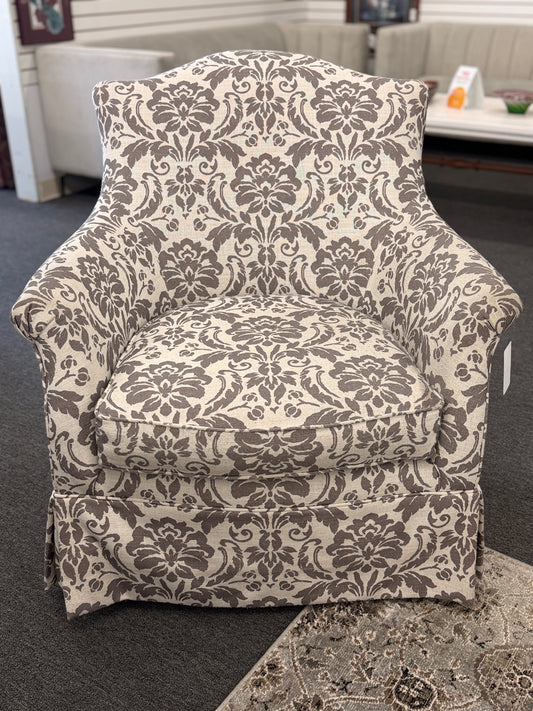 A traditional swivel armchair upholstered in a bold gray-and-cream floral damask pattern featuring a tailored base skirt in good condition.