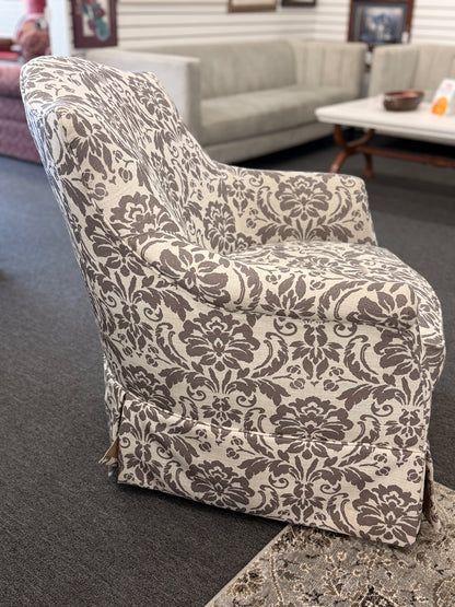 A traditional swivel armchair upholstered in a bold gray-and-cream floral damask pattern featuring a tailored base skirt in good condition.