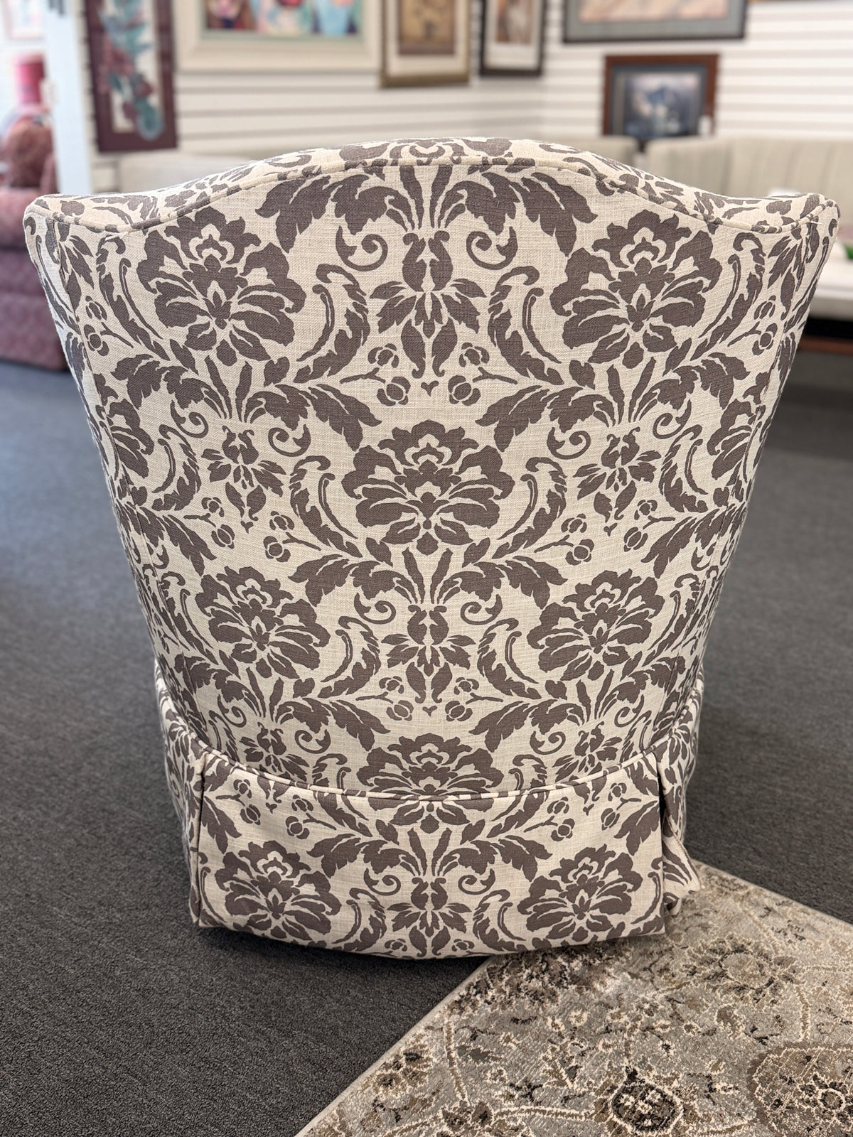 A traditional swivel armchair upholstered in a bold gray-and-cream floral damask pattern featuring a tailored base skirt in good condition.