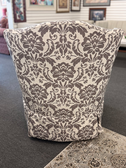 A traditional swivel armchair upholstered in a bold gray-and-cream floral damask pattern featuring a tailored base skirt in good condition.