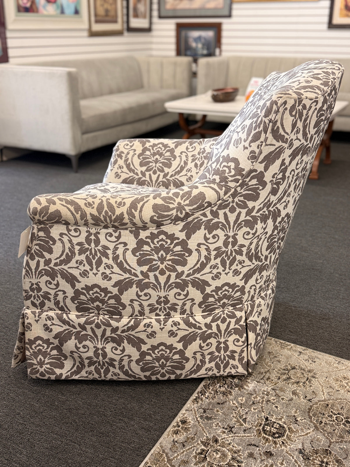 A traditional swivel armchair upholstered in a bold gray-and-cream floral damask pattern featuring a tailored base skirt in good condition.