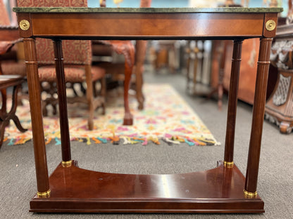 Traditional console table with a rectangular green marble top, dark wood frame, fluted cylindrical legs, gold-toned brass rosette accents, and a solid wood base plinth.