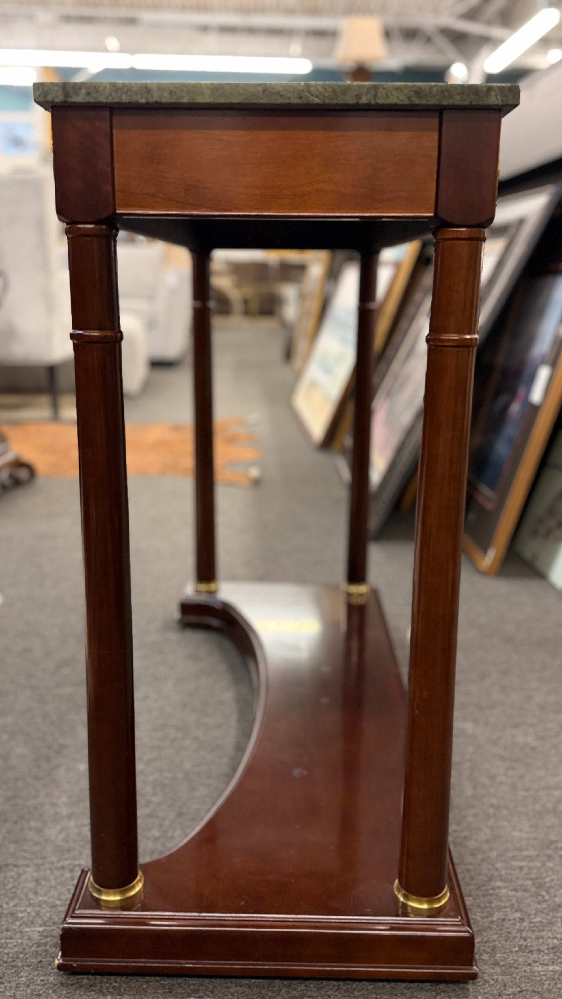 Traditional console table with a rectangular green marble top, dark wood frame, fluted cylindrical legs, gold-toned brass rosette accents, and a solid wood base plinth.