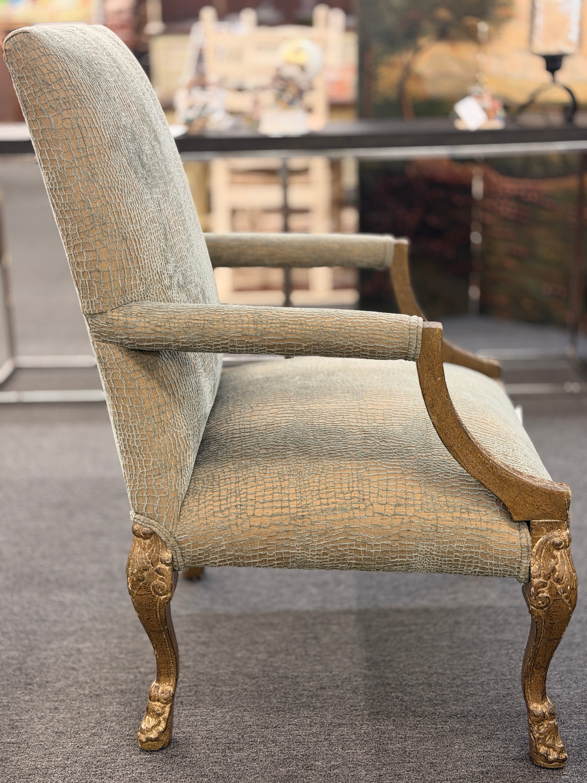 A high-back traditional accent armchair upholstered in a textured light-sage and gold fabric with gilded carved wooden arms, cabriole legs, and claw-and-ball feet in good condition.