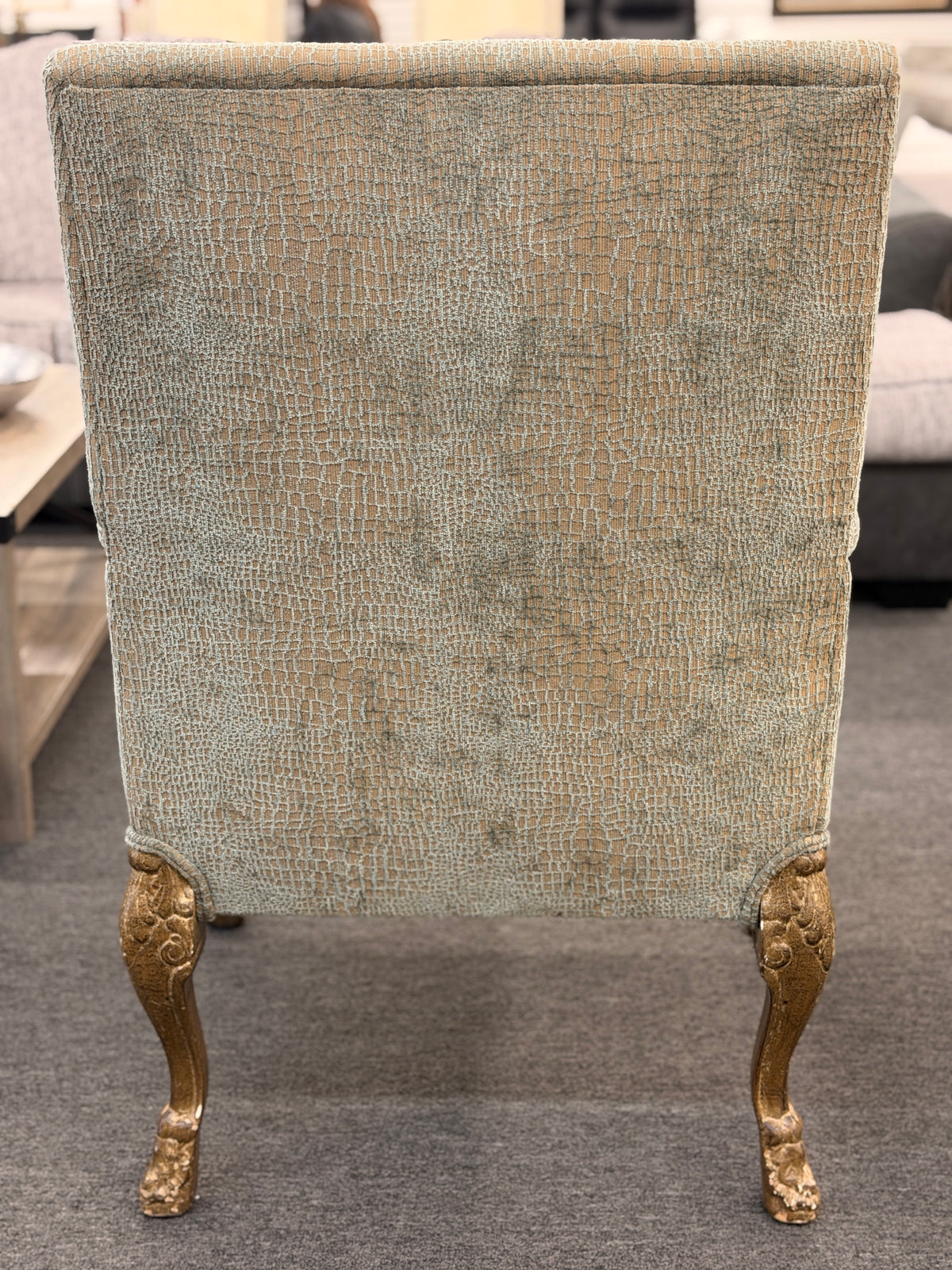 A high-back traditional accent armchair upholstered in a textured light-sage and gold fabric with gilded carved wooden arms, cabriole legs, and claw-and-ball feet in good condition.