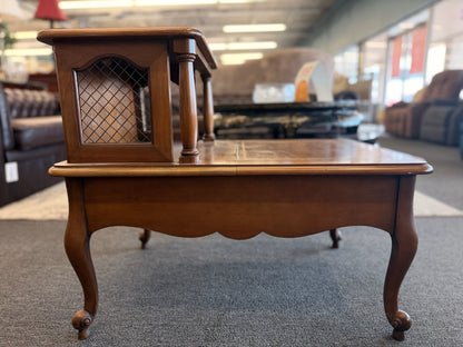 A wooden two-tiered step end table featuring decorative inlay with a gold border pattern, a single bottom drawer with ornate metal pulls, and cabriole legs.