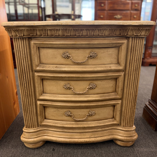 A traditional antique-style nightstand featuring a solid marble top, three serpentine-front drawers, fluted side pilasters, and an antiqued distressed painted finish.