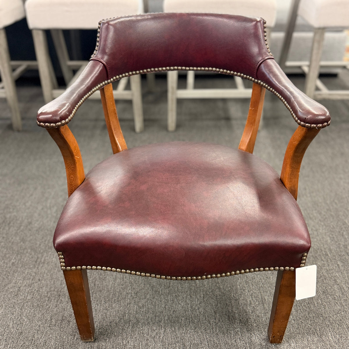 A traditional barrel-style captain's armchair upholstered in dark oxblood leather with nailhead trim and a curved natural wood frame in good condition.