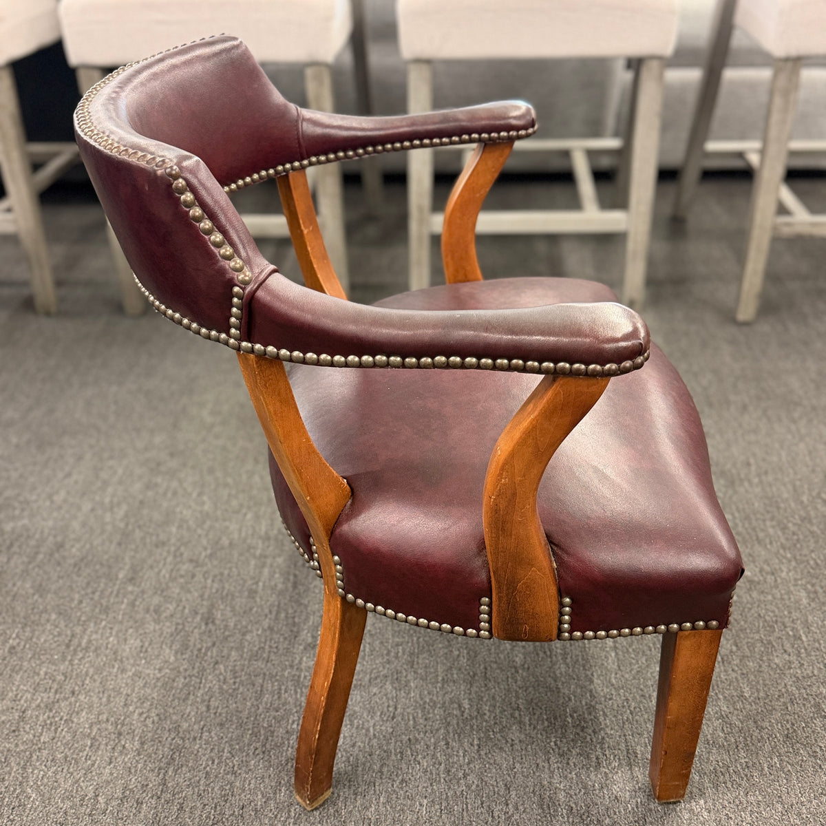 A traditional barrel-style captain's armchair upholstered in dark oxblood leather with nailhead trim and a curved natural wood frame in good condition.
