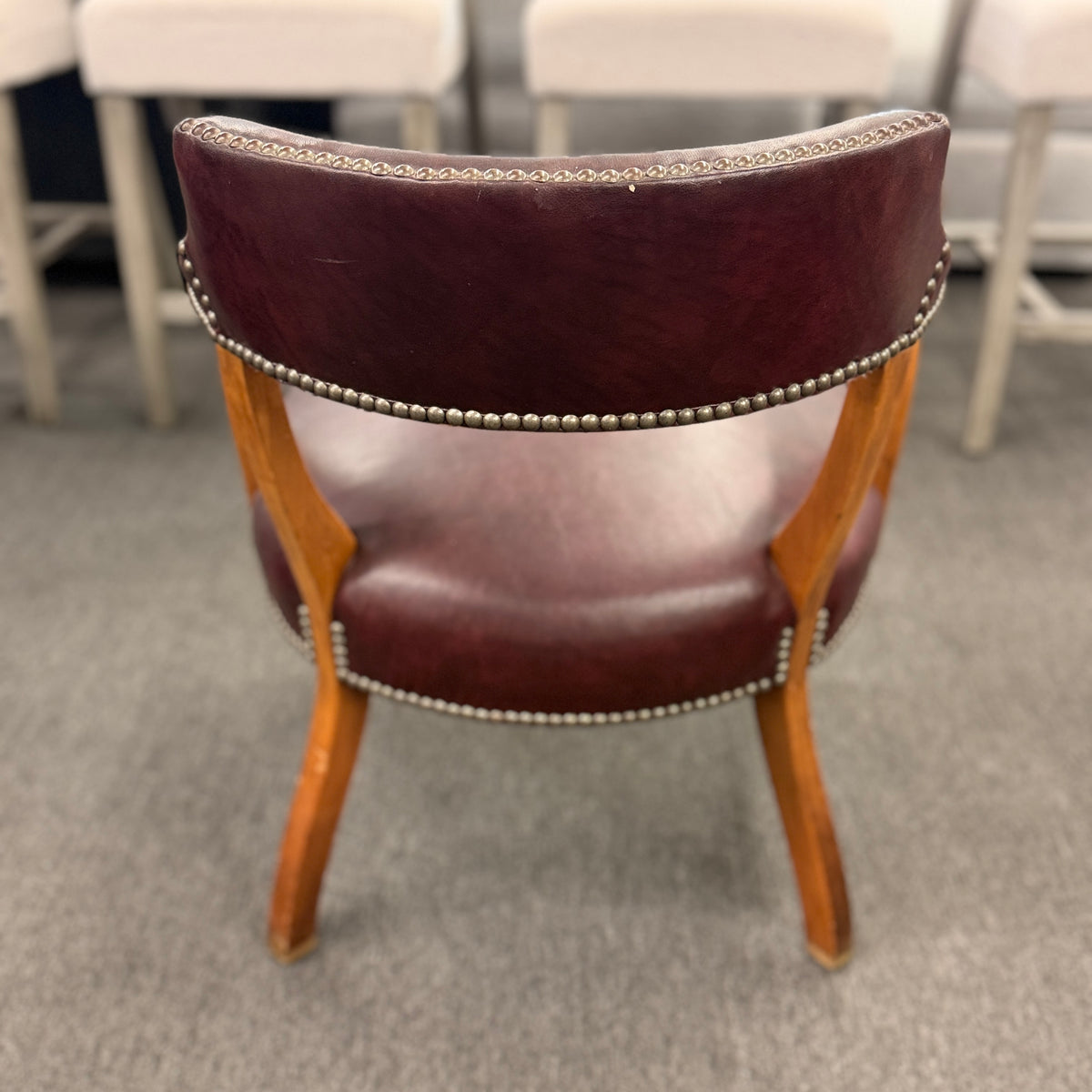 A traditional barrel-style captain's armchair upholstered in dark oxblood leather with nailhead trim and a curved natural wood frame in good condition.