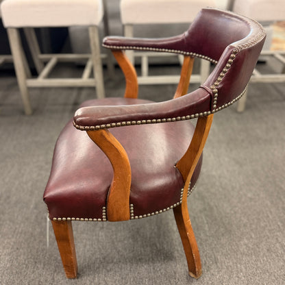 A traditional barrel-style captain's armchair upholstered in dark oxblood leather with nailhead trim and a curved natural wood frame in good condition.
