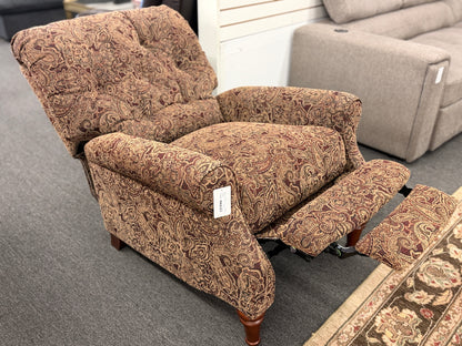 A traditional-style recliner armchair with rich brown and tan paisley upholstery, a tufted high backrest, rolled arms, and turned wooden legs in excellent condition.