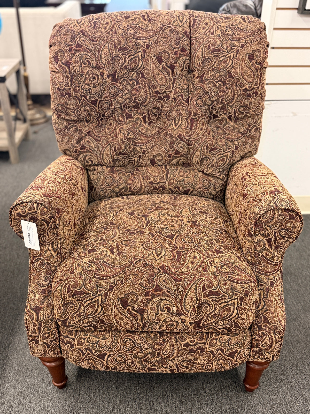 A traditional-style recliner armchair with rich brown and tan paisley upholstery, a tufted high backrest, rolled arms, and turned wooden legs in excellent condition.