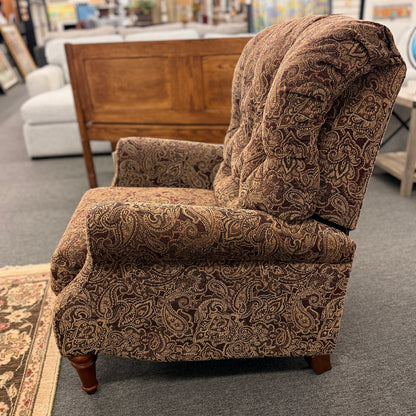 A traditional-style recliner armchair with rich brown and tan paisley upholstery, a tufted high backrest, rolled arms, and turned wooden legs in excellent condition.