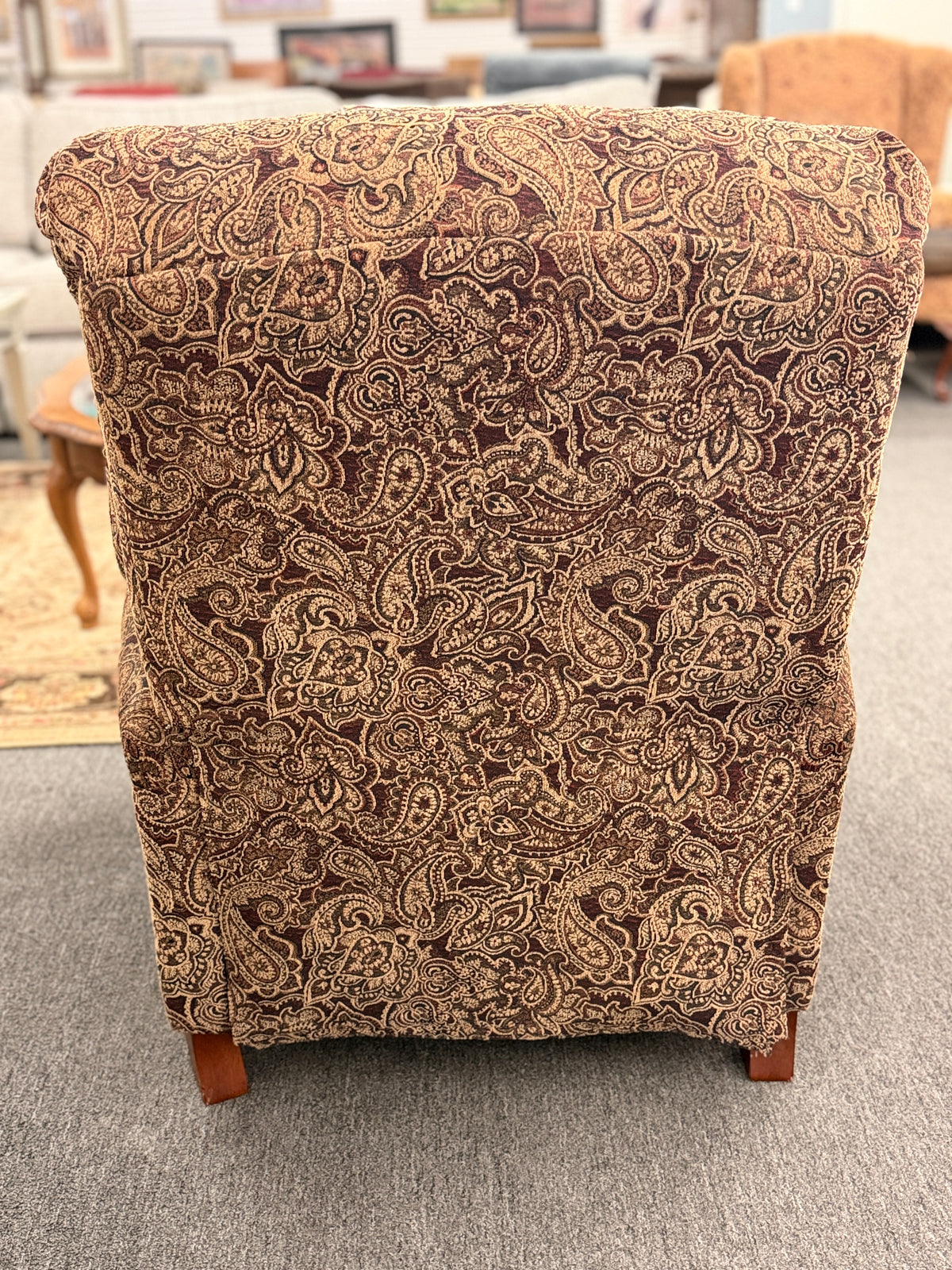 A traditional-style recliner armchair with rich brown and tan paisley upholstery, a tufted high backrest, rolled arms, and turned wooden legs in excellent condition.