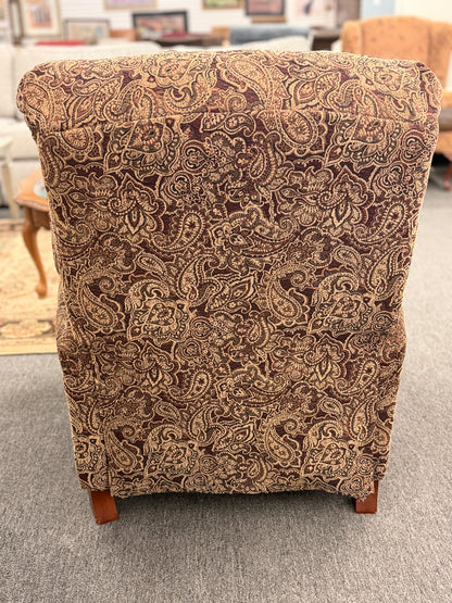 A traditional-style recliner armchair with rich brown and tan paisley upholstery, a tufted high backrest, rolled arms, and turned wooden legs in excellent condition.