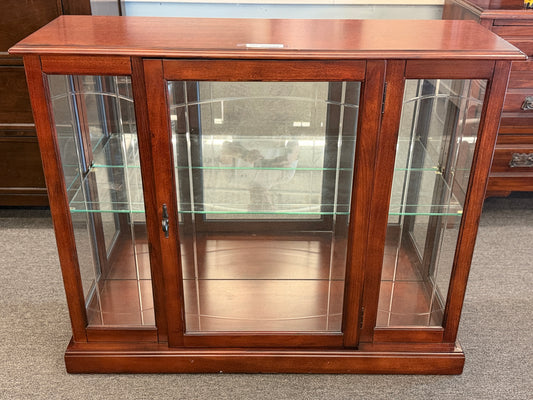 A traditional wooden display cabinet featuring glass doors, glass side panels, interior glass shelving, and a reddish-brown finish.