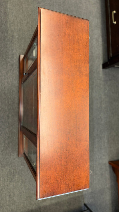 A traditional wooden display cabinet featuring glass doors, glass side panels, interior glass shelving, and a reddish-brown finish.