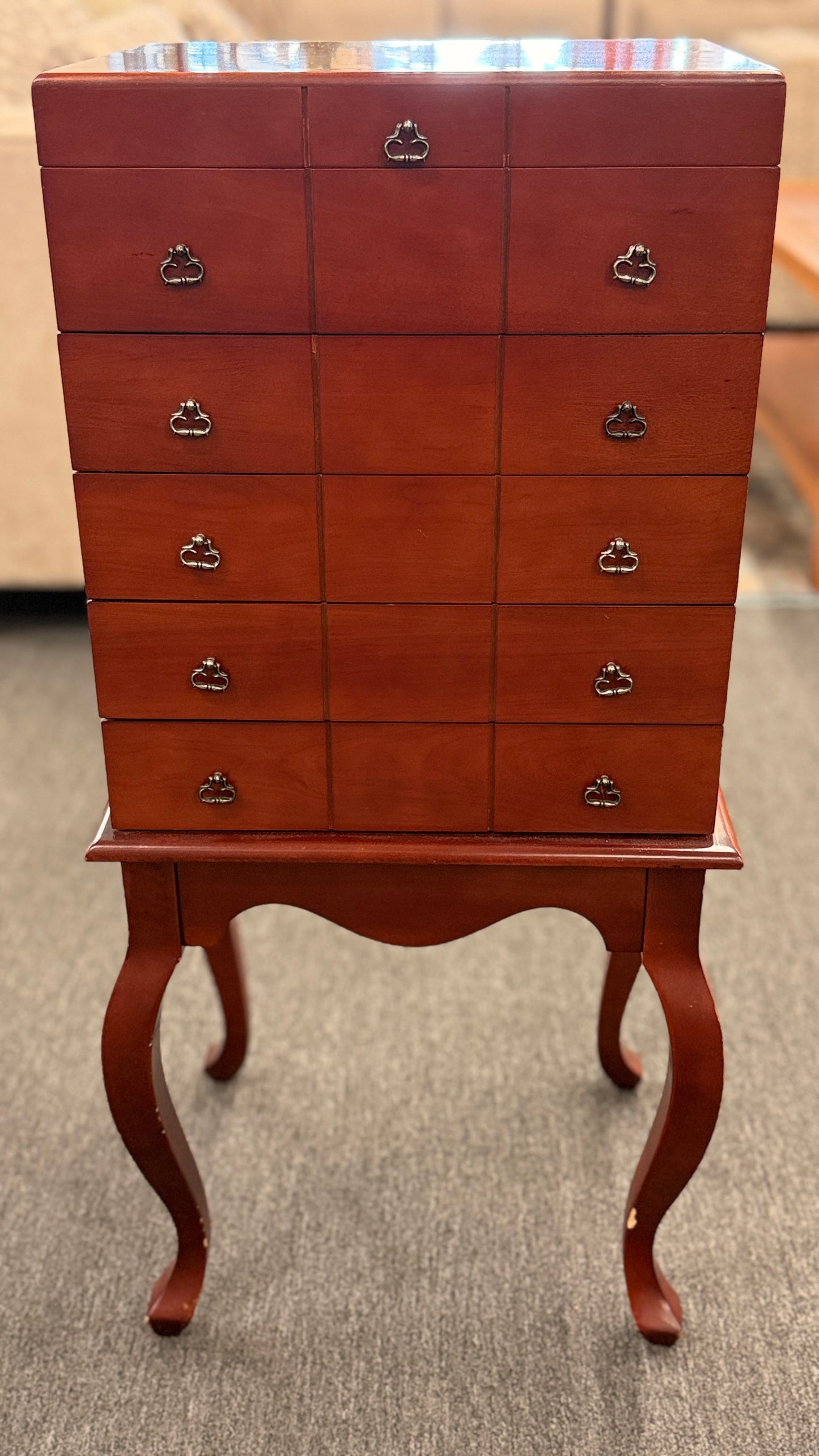 A tall, upright wooden jewelry or silverware chest shown open, revealing a ring-roll top compartment, five stacked drawers, burgundy fabric lining, and metal pulls.