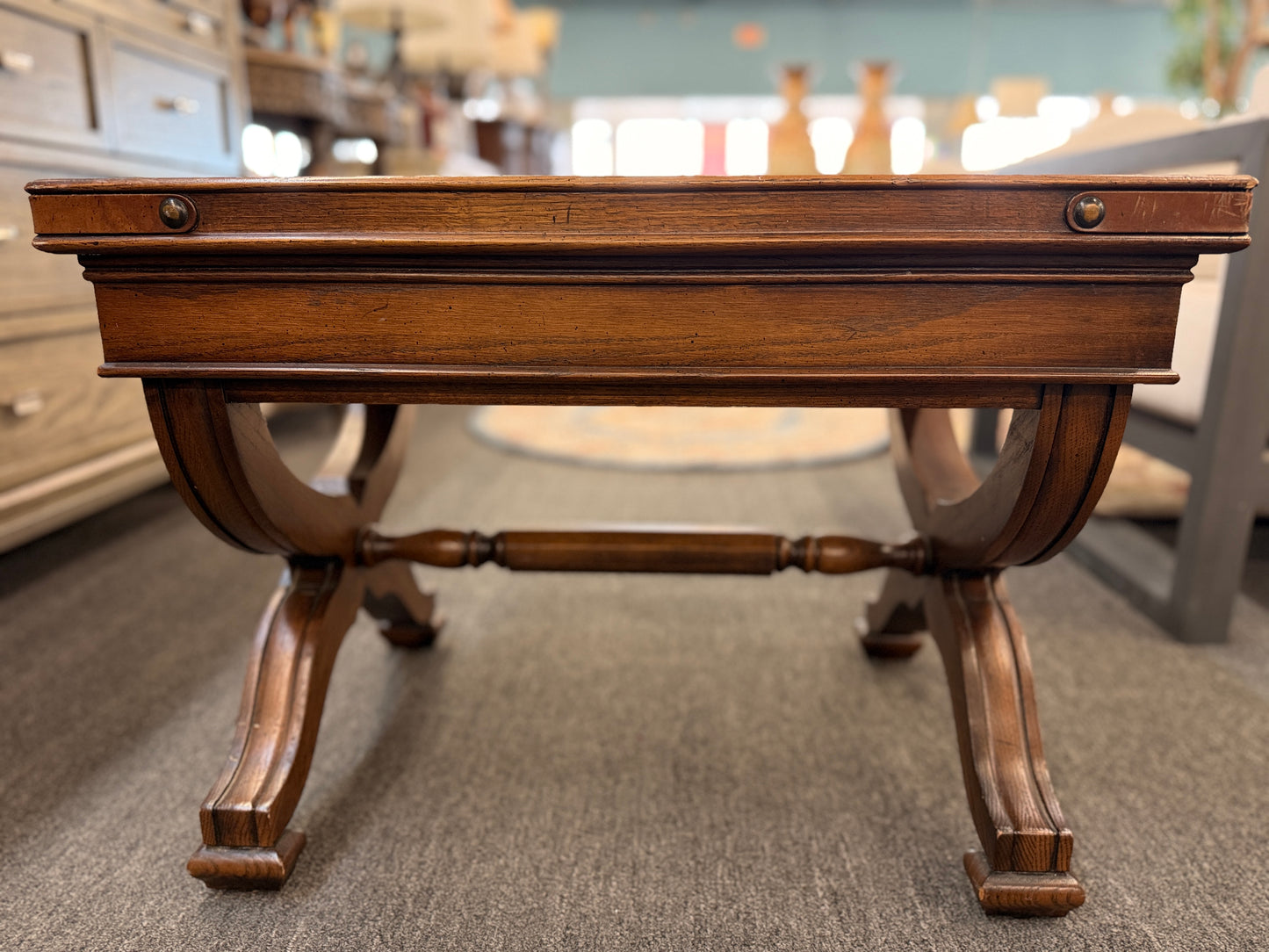 Traditional rectangular wood coffee table featuring a raised-edge tabletop, curved trestle-style legs, and decorative metal nailhead trim along the apron.