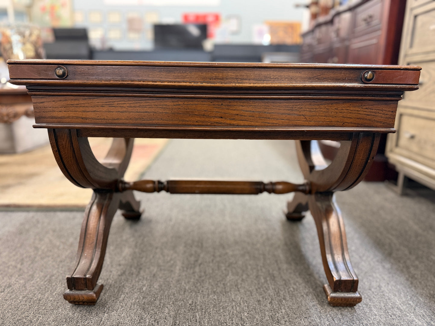 Traditional rectangular wood coffee table featuring a raised-edge tabletop, curved trestle-style legs, and decorative metal nailhead trim along the apron.