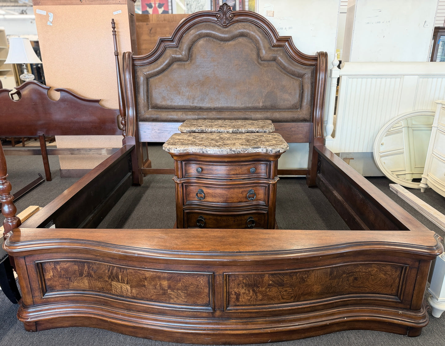 A grand wooden king bed frame flanked by two matching nightstands featuring marble tops.