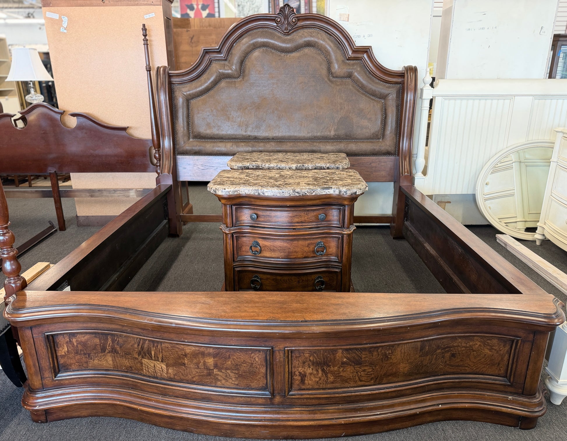 A grand wooden king bed frame flanked by two matching nightstands featuring marble tops.