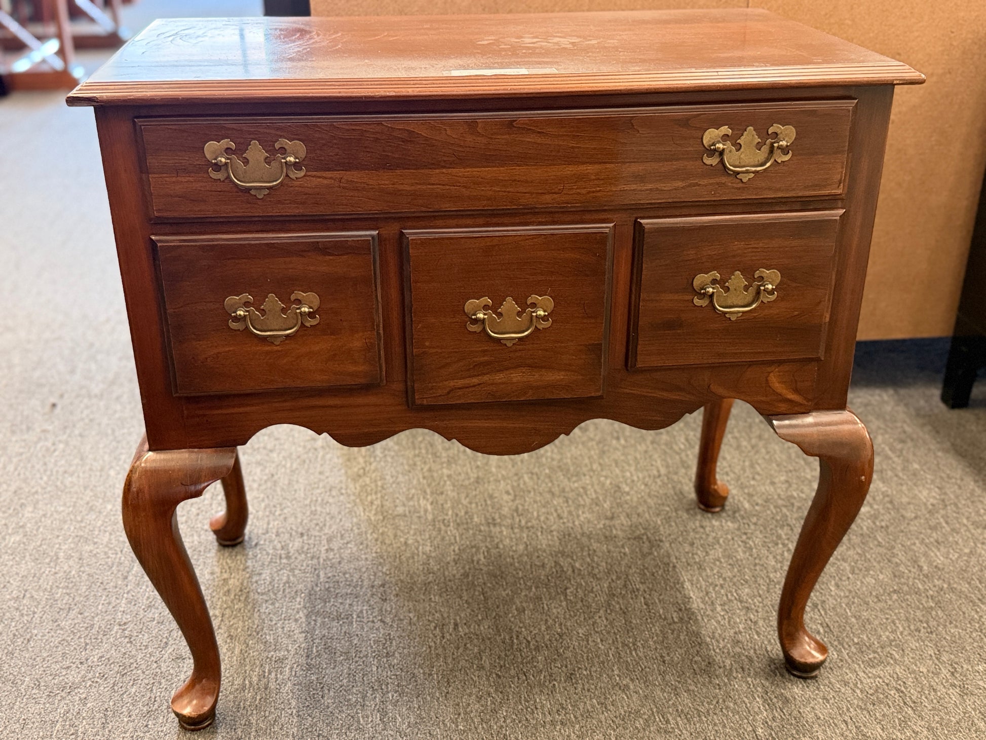 A traditional wooden lowboy accent dresser featuring four drawers with brass batwing drop pulls, a scalloped apron, and cabriole legs.