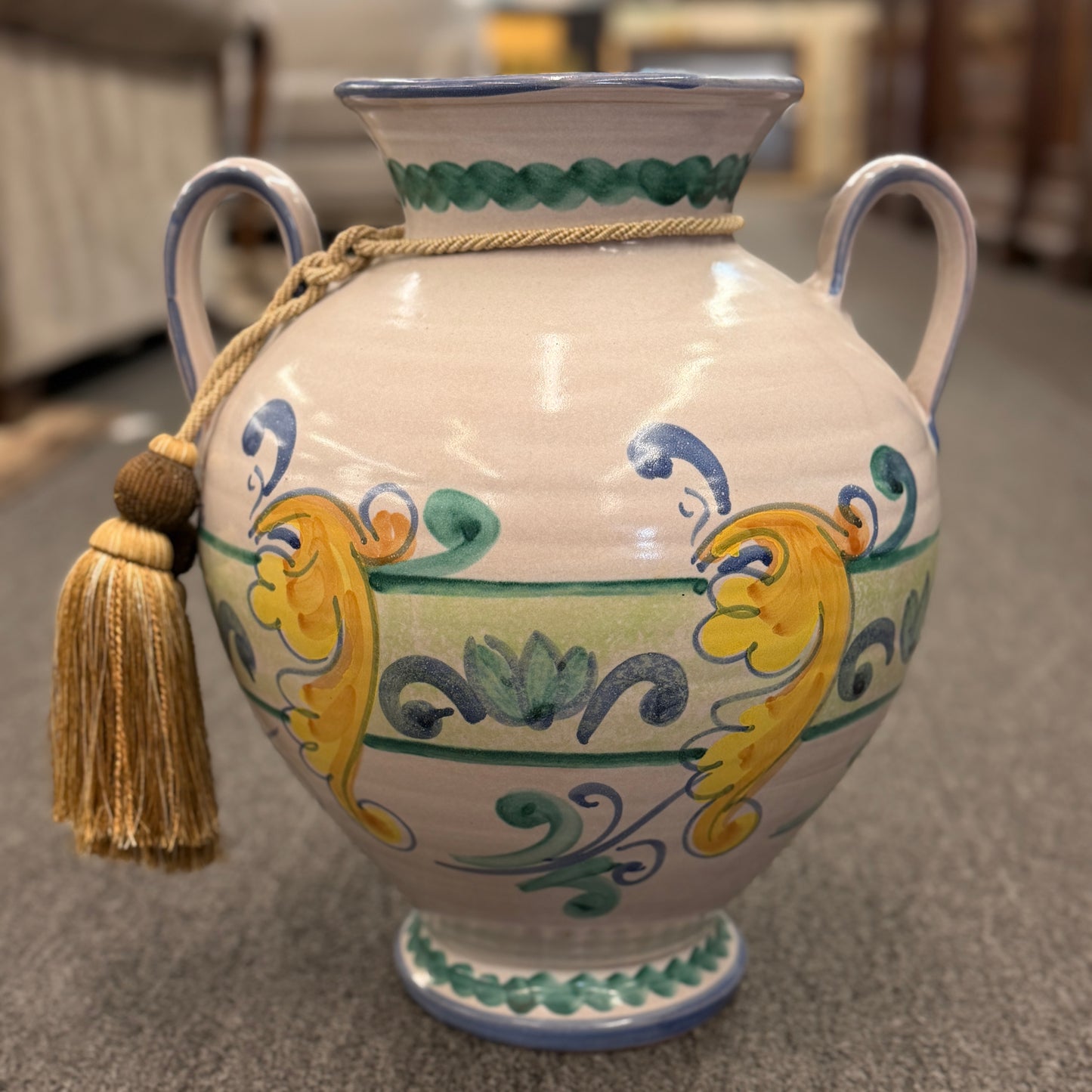 Tuscan farmhouse style ceramic floor and tabletop decorative vase featuring colorful patterns and a hanging tassel on a carpeted floor at 2nd Debut Houston consignment showroom
