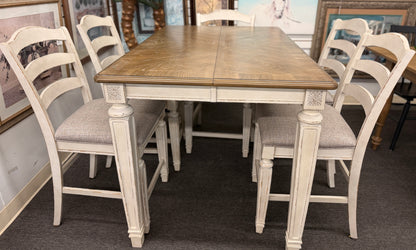 A two-tone counter-height dining set featuring a brown wood top rectangular table and six distressed white chairs with textured grey upholstered seats.